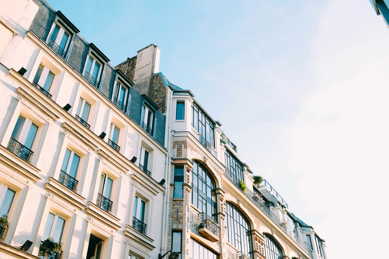 Immeuble haussmannien parisien, façade en pierre de taille, balcons en fer forgé et toit en zinc sous un ciel bleu.